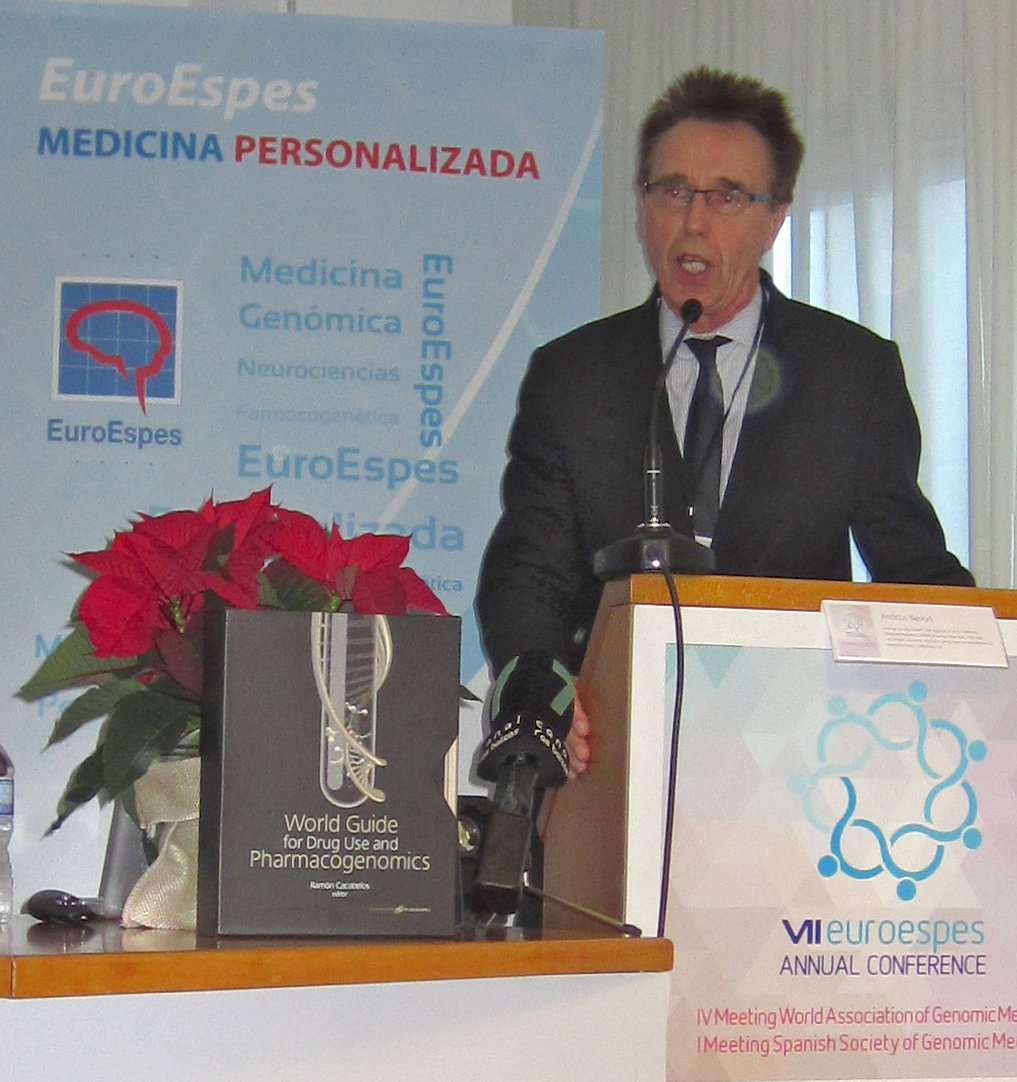 Un hombre con traje habla en un podio durante la Conferencia Anual de EuroEspes. A su lado hay una pancarta y una flor de pascua. El evento se centra en la medicina personalizada y la farmacogenómica.