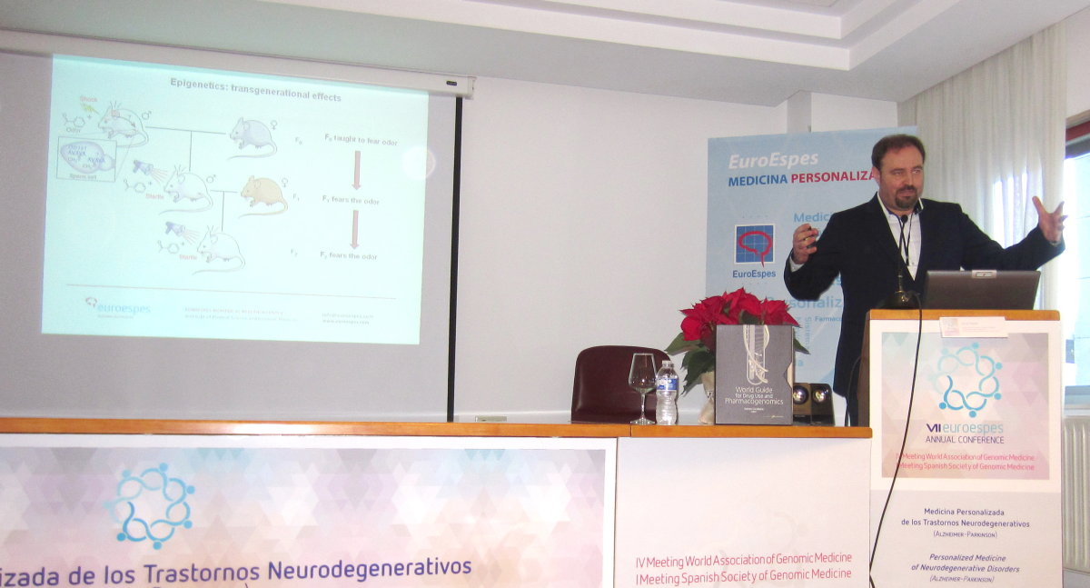 Un hombre habla en un podio durante una conferencia médica. Hay una diapositiva de presentación con diagramas de ratones relacionados con los efectos epigenéticos. El fondo muestra carteles de conferencias sobre trastornos neurodegenerativos y medicina personalizada.