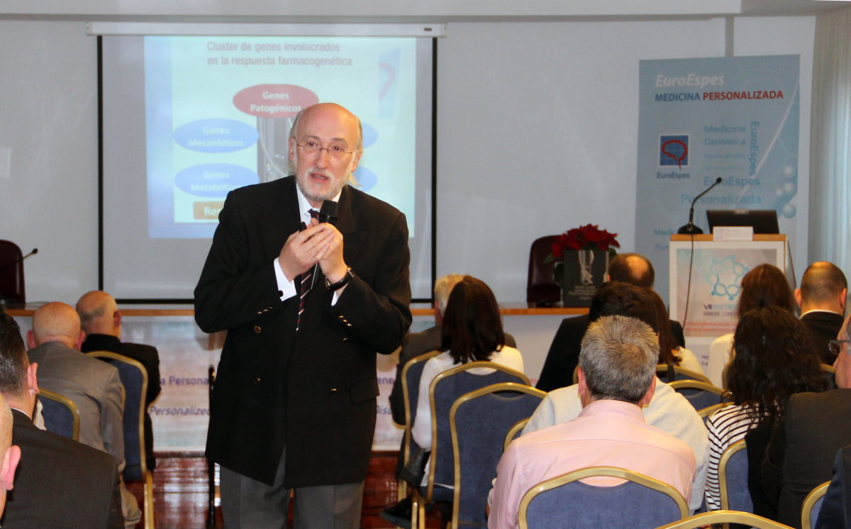 Un orador está dando una conferencia en una sala con asistentes sentados. Una pantalla muestra una diapositiva con diagramas y texto. El evento se centra en la medicina personalizada, como lo indica la señalización en el fondo.