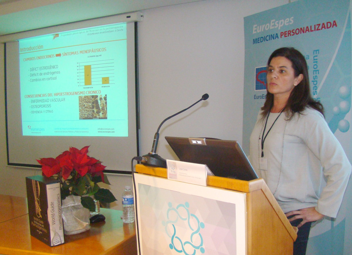 Una persona da una presentación sobre medicina personalizada. Se muestra una diapositiva sobre "Cambios endocrinos y síntomas menopáusicos". Sobre una mesa junto a ella hay una flor de pascua decorativa y un libro.