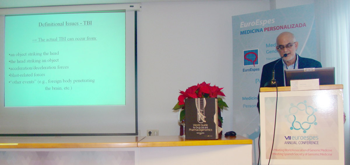 Un hombre da una presentación sobre traumatismo craneoencefálico en una conferencia. En la pantalla se muestran diapositivas que explican las diferentes causas del traumatismo craneoencefálico. El podio está decorado con un jarrón de flores rojas y una pancarta.