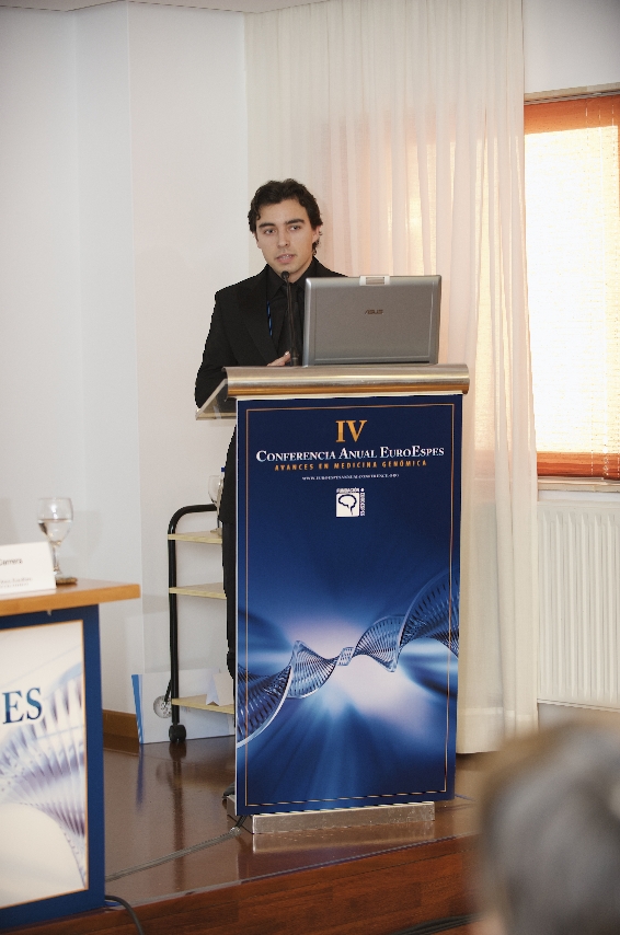 Una persona está de pie frente a un atril con un ordenador portátil, presentando una conferencia. El atril azul tiene un logotipo y el texto "Conferencia Anual EuroEspes". La sala es luminosa y la luz natural entra por una ventana.