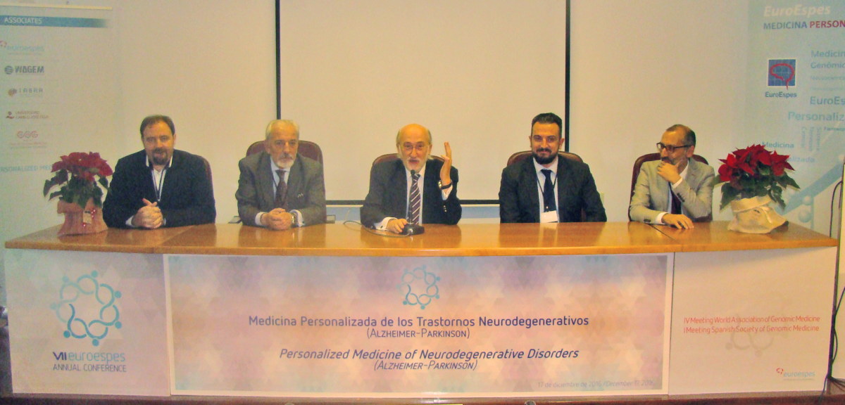 Cinco hombres están sentados detrás de una mesa larga en un panel de conferencias. Una pancarta sobre la mesa dice "Medicina personalizada de los trastornos neurodegenerativos: Alzheimer-Parkinson". También se ven una pantalla y plantas en macetas en la sala.