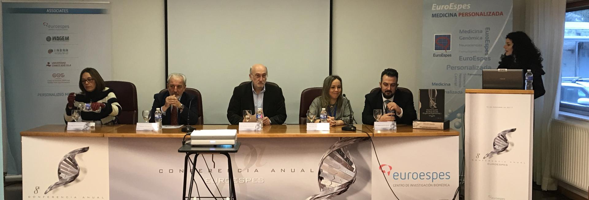 Un panel de cinco personas está sentado en una mesa larga con micrófonos y botellas de agua. Una mujer está de pie en un podio a la derecha. La mesa está cubierta con una pancarta que muestra "EuroEspes" y "Conferencia Anual".