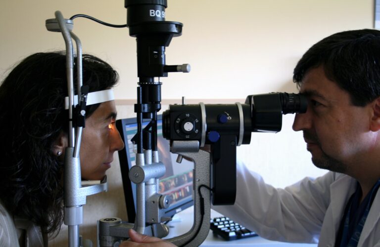 En un contexto clínico de neurooftalmología, un oftalmólogo utiliza una lámpara de hendidura para examinar minuciosamente el ojo de un paciente. El paciente apoya su barbilla sobre el dispositivo mientras el médico utiliza un equipo especializado para realizar una observación precisa.