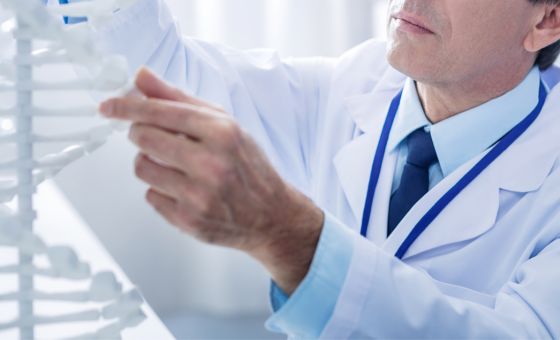 Un científico con bata de laboratorio examina un modelo de ADN, centrándose en la estructura de doble hélice, sugiriendo una investigación para el Boletín Médico EuroEspes Salud en un entorno de laboratorio.