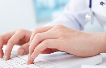 Una persona con bata blanca escribe en un teclado blanco, lo que sugiere que se trata de un profesional médico que actualiza el Boletín Médico. El fondo está difuminado y se centra en las manos y el teclado, lo que enfatiza la precisión en la introducción de datos de EuroEspes Health.